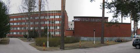 Centrallaboratoriets byggnad av rött tegel kantas av höga tallar.