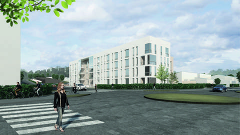 Vit ny bostadsbyggnad bakom cirkulationsplatsen. I förgrunden går en människa över övergångsstället.