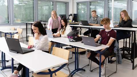 Opiskelijat istuvat luokassa tietokoneidensa ääressä