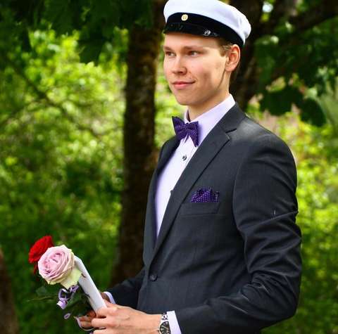 Severi poseeraa ulkona ylioppilaslakki päässä ja ruusu kädessä.