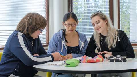 Kolme Tapiolan lukion opiskelijaa istuu ja keskustelee pöydän ääressä. 