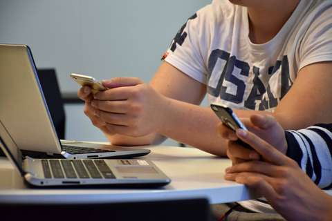 Händerna av två unga människor med mobiltelefoner. Bärbara datorer på bordet.