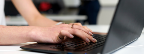 Henkilö kirjoittaa tietokoneella.