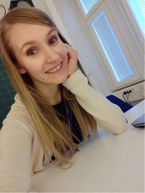 Susanna istuu opettajanpöydän ääressä ja hymyilee kameralle.