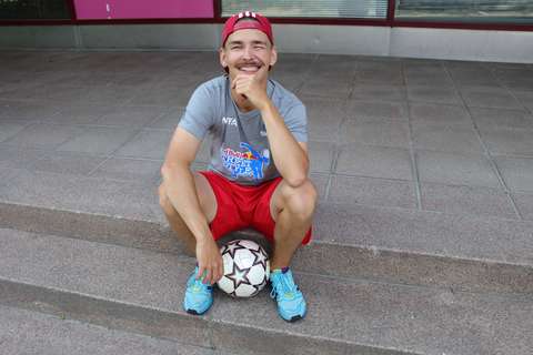 Valokuvassa nuori mies urheiluasussa istuu rappusilla, jaloissa jalkapallo.