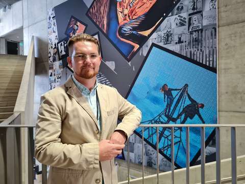 Jere Juutilainen nojaa kaiteeseen sisätiloissa Opinmäessä. Taustalla akustinen seinä, joka koostuu oppilaiden ottamista valokuvista.