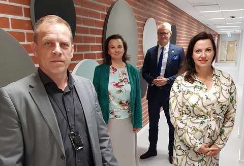 Kaksi miestä ja kaksi naista seisovat käytävässä ja katsovat kameraan.