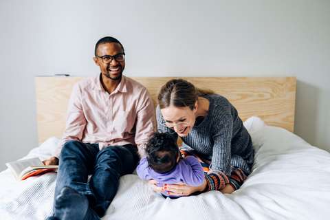 Vanhemmat ja lapsi istuvat sängyllä. 