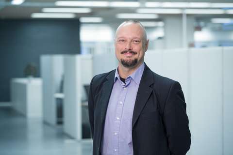 Hymyilevä mies seisoo kädet selän takana.