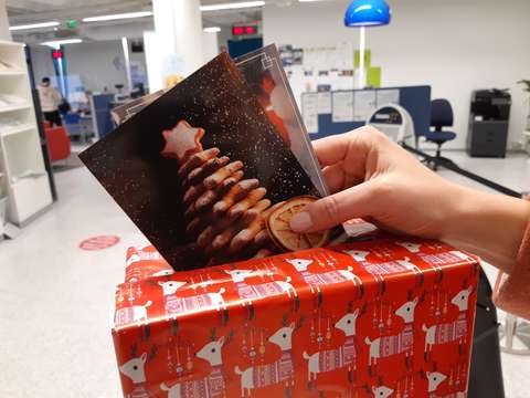 A hand is putting Christmas cards in a box which is wrapped in Christmas paper.