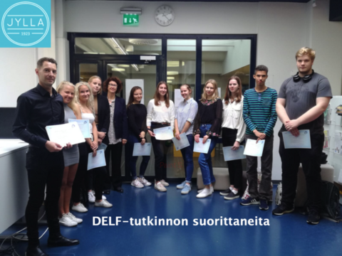 Kuvassa on Espoonlahden lukion opiskelijoita, jotka ovat saaneet DELF-tutkinnon suoritettua. Opiskelijoilla on tutkintotodistukset kädessä. Kuvassa on valkoinen teksti, jossa lukee DELF-tutkinnon suorittaneita. Vasemmassa yläkulmassa on Espoonlahden lukion logo.