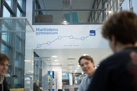 Tre studerande sitter och pratar under texten Mattlidens gymnasium, read, lead, succeed