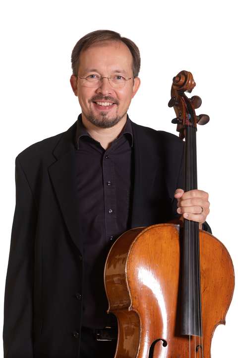 Cellisten håller i en cello och ler.