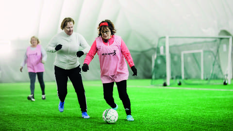 Kolme henkilöä pelaamassa jalkapalloa kuplahallissa.