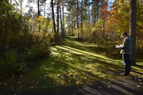 Miespuolinen arkeologi katsoo karttakuvaa polun varrella.