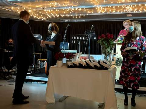 Uusille ylioppilaille jaetaan kuvassa todistukset ja lakit. 