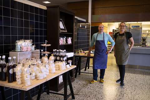 Kaksi henkilöä seisoo keittiötilojen edessä hymyillen.