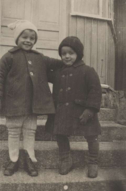 Kaksi pientä poikaa portailla seisomassa kädet toistensa olkapäillä.