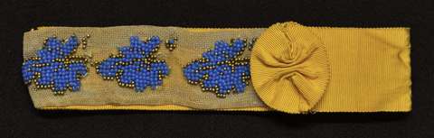 Keltainen morsiussukkanauha, sinisillä ja kultaisilla helmillä koristeltu.