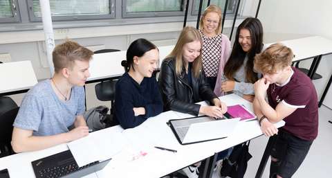 Opiskelijat istuvat pöydän ääressä ja katsovat tietokoneruutua.