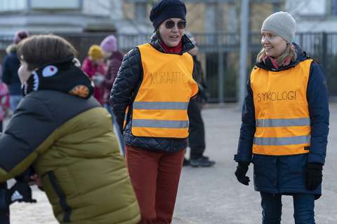 School psychologist and school social worker at recess wearing safety vests. There are children playing around them.