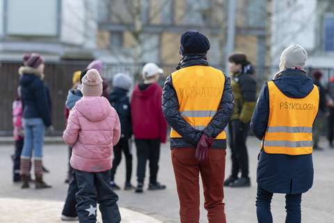 School psychologist and school social worker at recess wearing safety vests. There are children playing around them. 