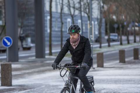 Pyöräilijä pyöräilee kypärä päässään lumisella ja hiekoitetulla kadulla.