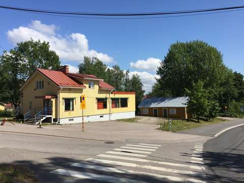 Keltainen puurakennus Kadun kulmassa kesäinen aurinko paistaa.