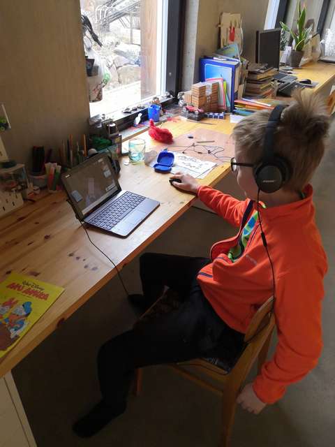 Poika pöydällä olevan läppärin ääressä kuulokkeet korvillaan.