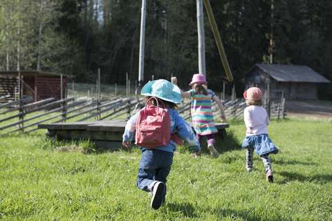 Lapsia juoksemassa kesäisellä nurmella maaseutupihapiirissä.