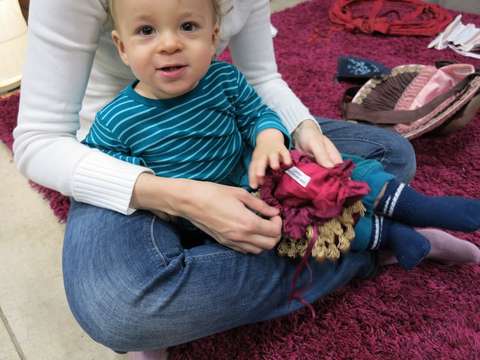 Lapsi katsoo kameraan aikuisen sylistä.He istuvat matolla ja leikkivät jotain.