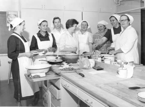 Suurkeittiöhenkilökuntaa pöydänääressä huiveissaan ja essuissaan
