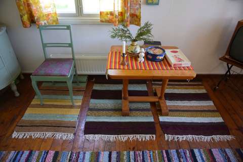 Huoneen seinää vasten tuoli ja pöytä, lattialla räsymattoja.