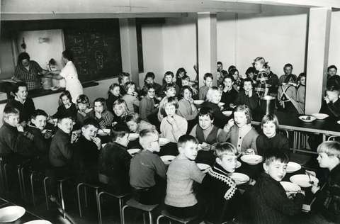 Koululaisia koulun ruokalassa. Mustavalkokuva.