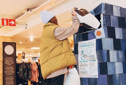 Nainen laittaa muovipussia poistotekstiilien keräyslaatikkoon.