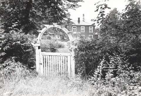 Kuvassa pihaportti jonka taustalla puiden välissä pilkottaa kartano.