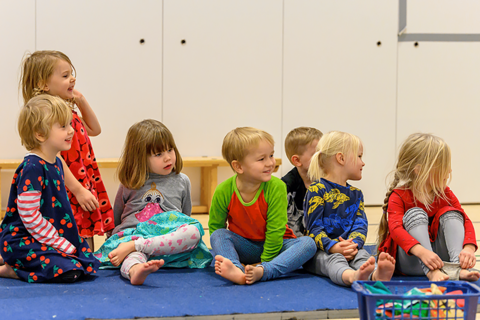 Approximately 5-year-old children are sitting in the sports room and following somenting interesting.