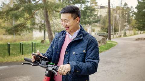 Hymyilevä mies skuutin kanssa selaa kännykkää