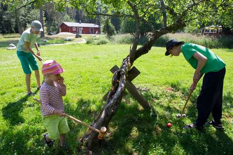 Lapset ja nuoret pelaavat puistossa krokettia kesäisessä kelissä.