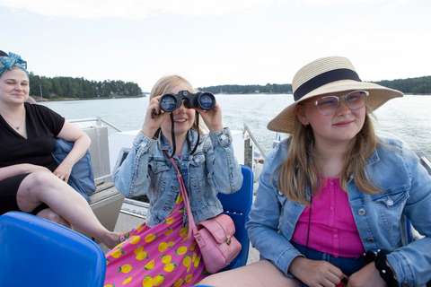 Nainen ja kaksi teinityttöä veneessä, yksi teinitytöistä kiikaroi merelle.