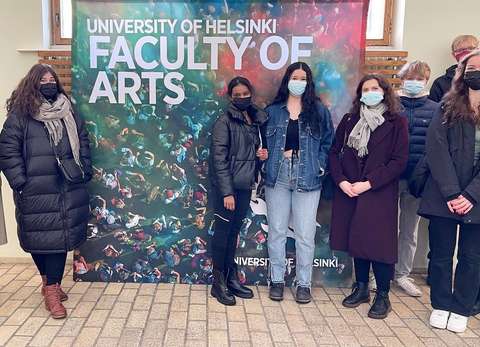 Opiskelijat seisovat kyltin edessä Aalto-yliopistolla.