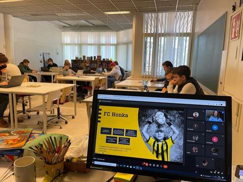 Kuva luokasta, jossa näkyy tietokoneen ruutu ja opiskelijoita luokassa.