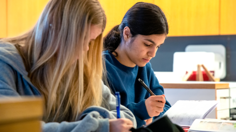 Kaksi yläkoululaista oppilasta tekevät koulutehtäviä pöydän ääressä.