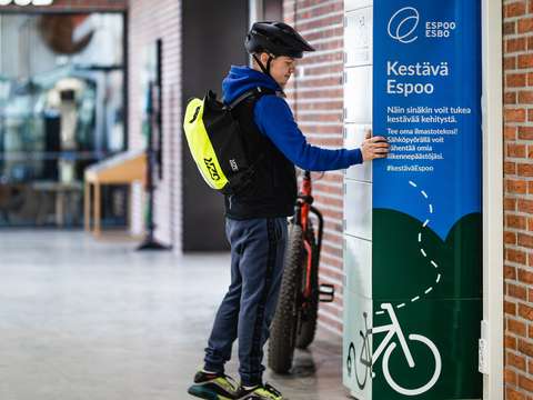 Paloturvallisen latauskaapin sähköpyörien akkujen lataamiseen Otaniemessä ja pyöräilijä avaamassa kaappia.