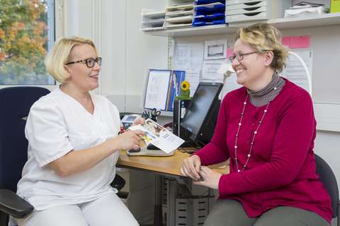 Valokuva, jossa pöydän ääressä kaksi henkilöä. Vasemmalla lääkäri, joka näyttää esitettä asiakkaalle.