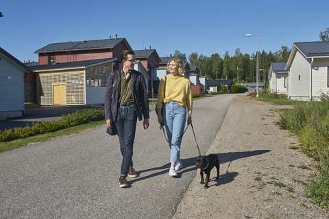  En kvinna och en man går med en hund i ett småhusområde.