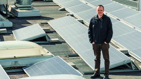  A man is standing on the roof in the middle of the solar panels.