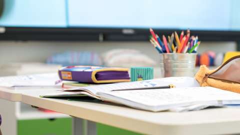 Vihko, kyniä ja penaali pulpetilla.