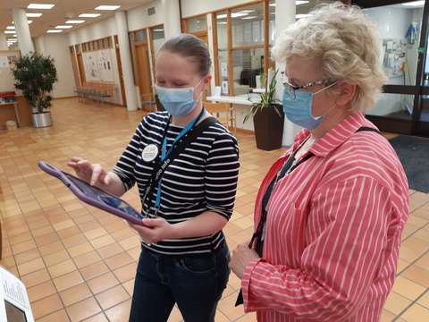  Two people are standing and one is showing the other something on the tablet.