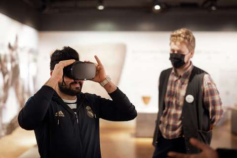 Henkilö katsoo VR-laseilla, ja taustalla museo-opas seuraa.